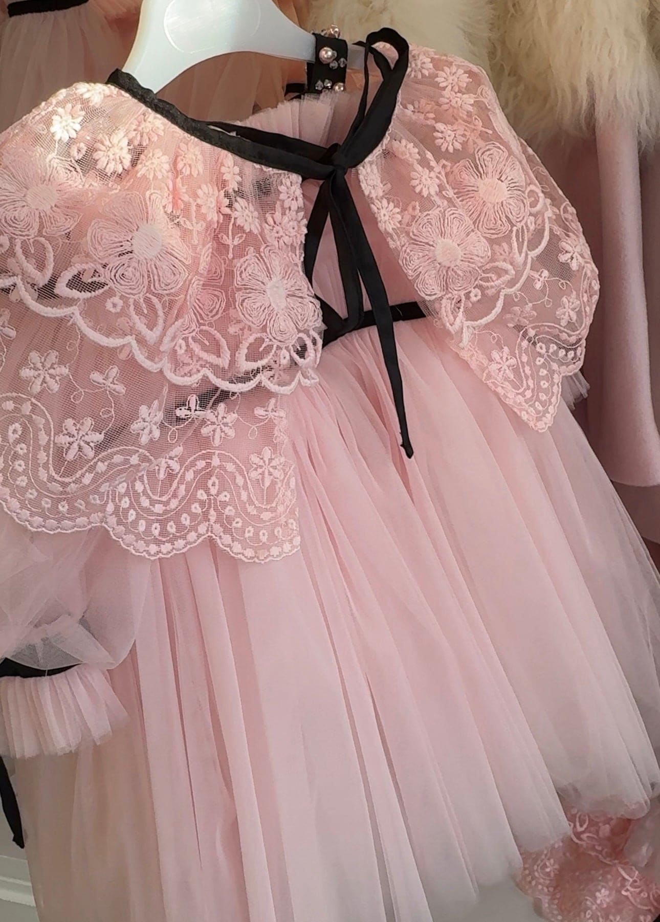 Close up of blush pink lace cape accessory with a black waist bow detail, highlighting the texture and pattern of the lace