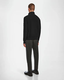 A man stands facing away from the camera, wearing the Rudsak EUGENE - 6124016 Black hybrid jacket, dark gray trousers, and black shoes against a plain white background.