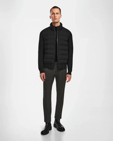 A man stands against a white background, wearing the Rudsak EUGENE - 6124016 Black jacket over a black shirt, paired with dark brown pants and black boots. He faces forward with his arms relaxed at his sides.