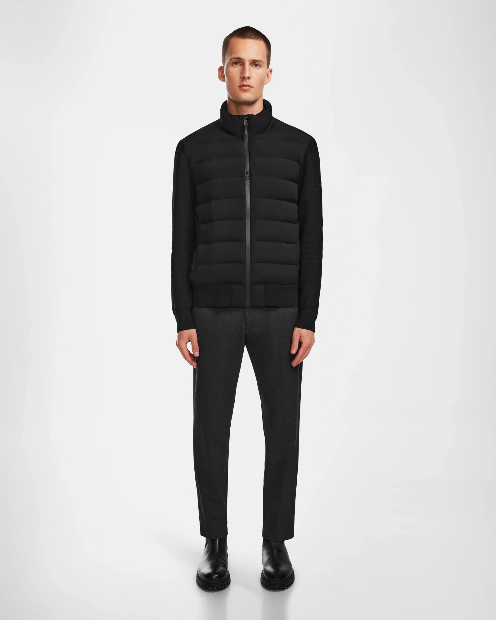 A man faces forward wearing the Rudsak EUGENE - 6124016 Black lightweight mixed-media jacket, paired with dark gray pants and black shoes, set against a plain white background.