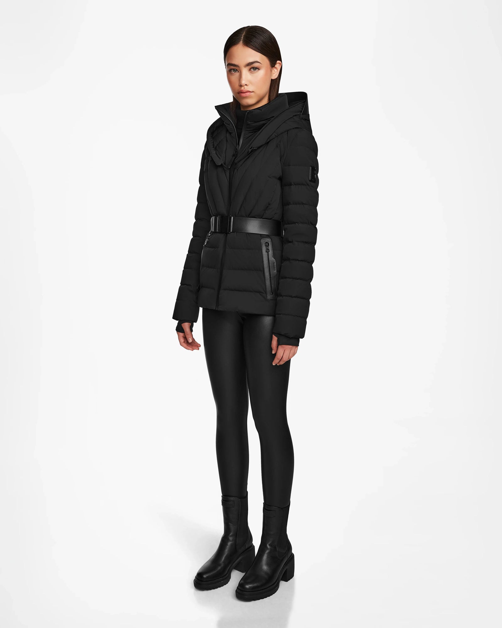 A woman wearing the Rudsak ALISA - L124506 Black quilted down puffer with a vegan leather belt.