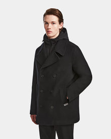 A young man wears the ARTHUR - 6124521 Black peacoat by Rudsak, crafted from a premium wool blend, with dark pants. He stands against a plain light background, looking straight ahead with one hand in his pocket.