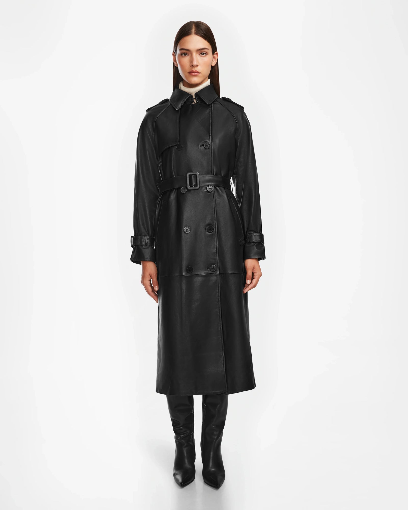 A woman faces forward in a sleek Rudsak CASSIE L - 8124531 Black leather trench coat with a belted waist, paired with knee-high black boots against a plain white background.