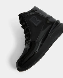 The Rudsak CHELSA - L224505 Black is a women’s black high-top sneaker boot with glossy and matte finishes, black laces, a bold “R” side logo, and a waterproof zipper. Shown angled to reveal the side and sole against a white background.