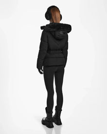 A person with long, straight hair wears black earmuffs, gloves, leggings, lace-up boots, and the Rudsak CHRISTELLE M - L123525 Black women's quilted down puffer with fur-lined hood and fitted silhouette, facing away on a white background.