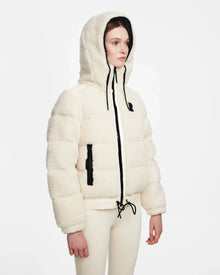 A person models the Rudsak DANI S - 8124537 Iceland: a white, hooded, cropped ski jacket with black drawstrings and beige pants, standing against a plain white background and looking slightly to the side.