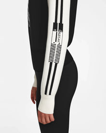 A woman models the Rudsak FANNY - 8524506 Black knit pullover with black and white graphic design and 1944 SPORT sleeve text, perfect for winter layering or après-ski, shown from the side against a plain white background.