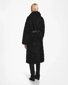 A person with straight blonde hair faces away, wearing the KAMILAH - 8124827 Black womens faux fur trench by Rudsak, styled with a vegan leather belt and tall black boots against a plain white background.