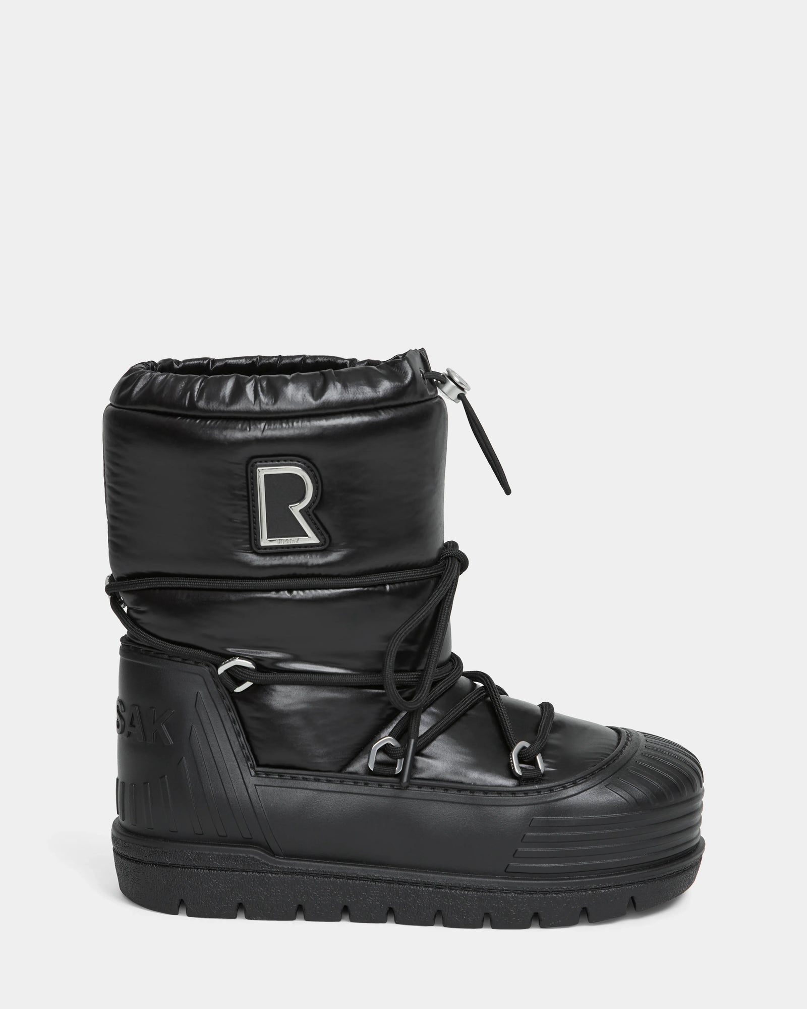 The KIKA - L224506 Black by Rudsak is a women's black high-top winter boot with a chunky rubber sole, quilted upper, lace-up front, drawstring closure, and an "R" patch—ideal for fashion-forward winter style.