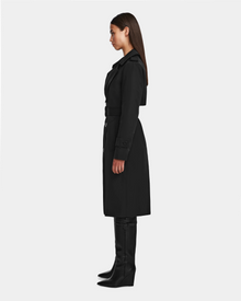 A woman in profile stands against a plain background, wearing the KINDA - 8124690 Black trench coat by Rudsak and tall black boots. Her straight hair falls past her shoulders.
