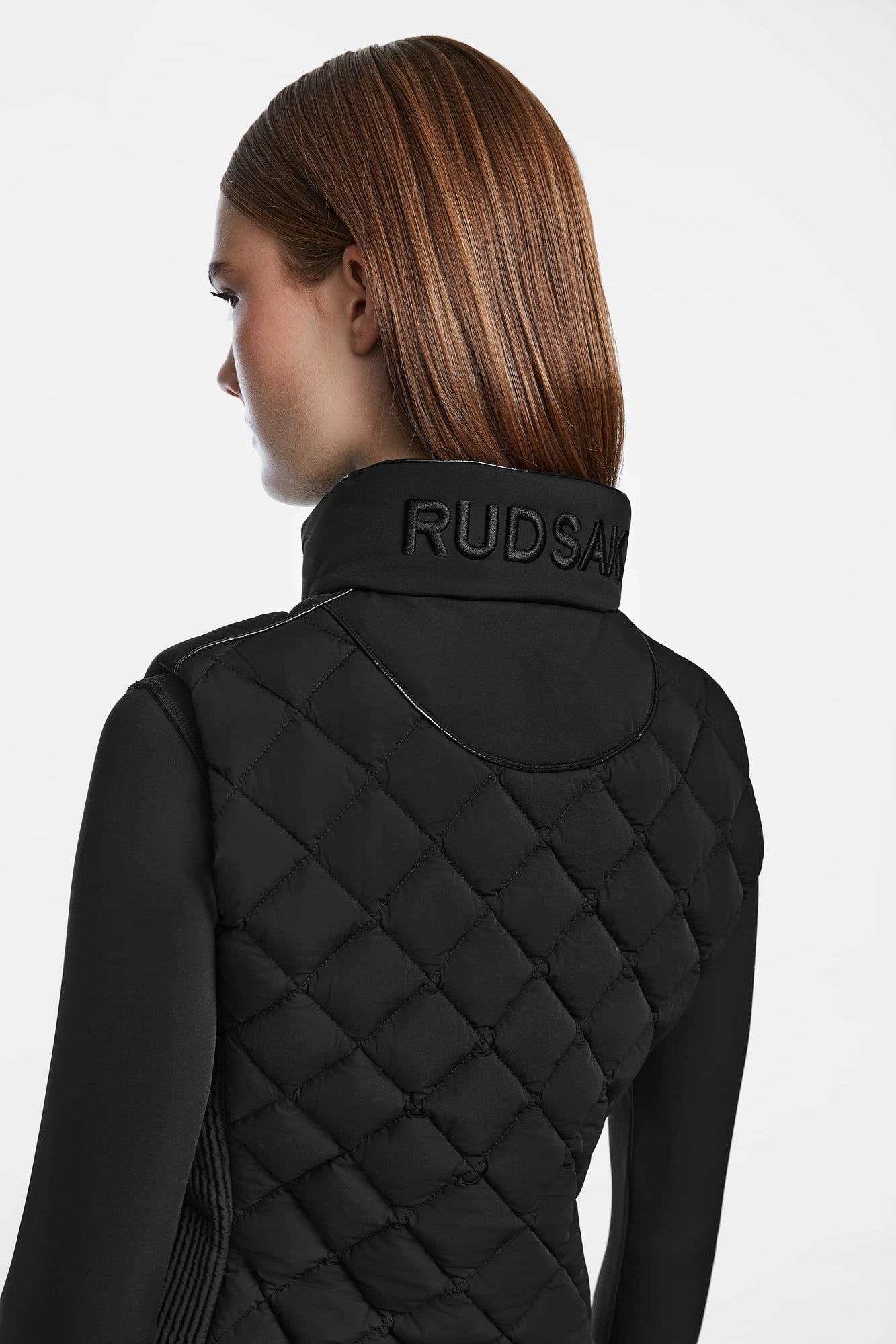 A woman with straight, light brown hair is shown from the back, wearing the Rudsak MATILDA - L124504 Black quilted jacket with an embroidered collar, set against a plain white background.
