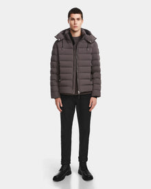 A man faces forward wearing the Rudsak NAVAN - 6124551 Grey mens quilted down puffer, wind and water-repellent, paired with black pants and black boots against a plain white background.