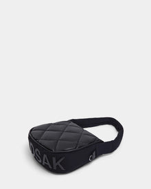 The Rudsak NIOBE L - 8324503 Black sling bag, quilted with a padded strap, is shown on a plain light background. Bold “DSAK” lettering appears prominently on the side.