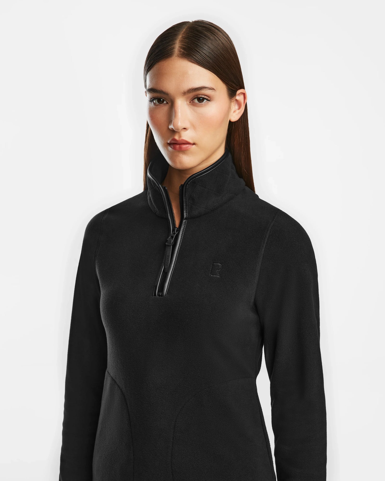 A woman with straight brown hair models the Rudsak ORCHID - 8524616 Black women’s half-zip pullover polar fleece sweater with vegan leather trims, standing against a plain white background and looking at the camera.