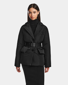 A woman with long dark hair wears the Rudsak PAOLA - 8124547 Black down blazer over a black turtleneck and skirt, standing against a plain white background.