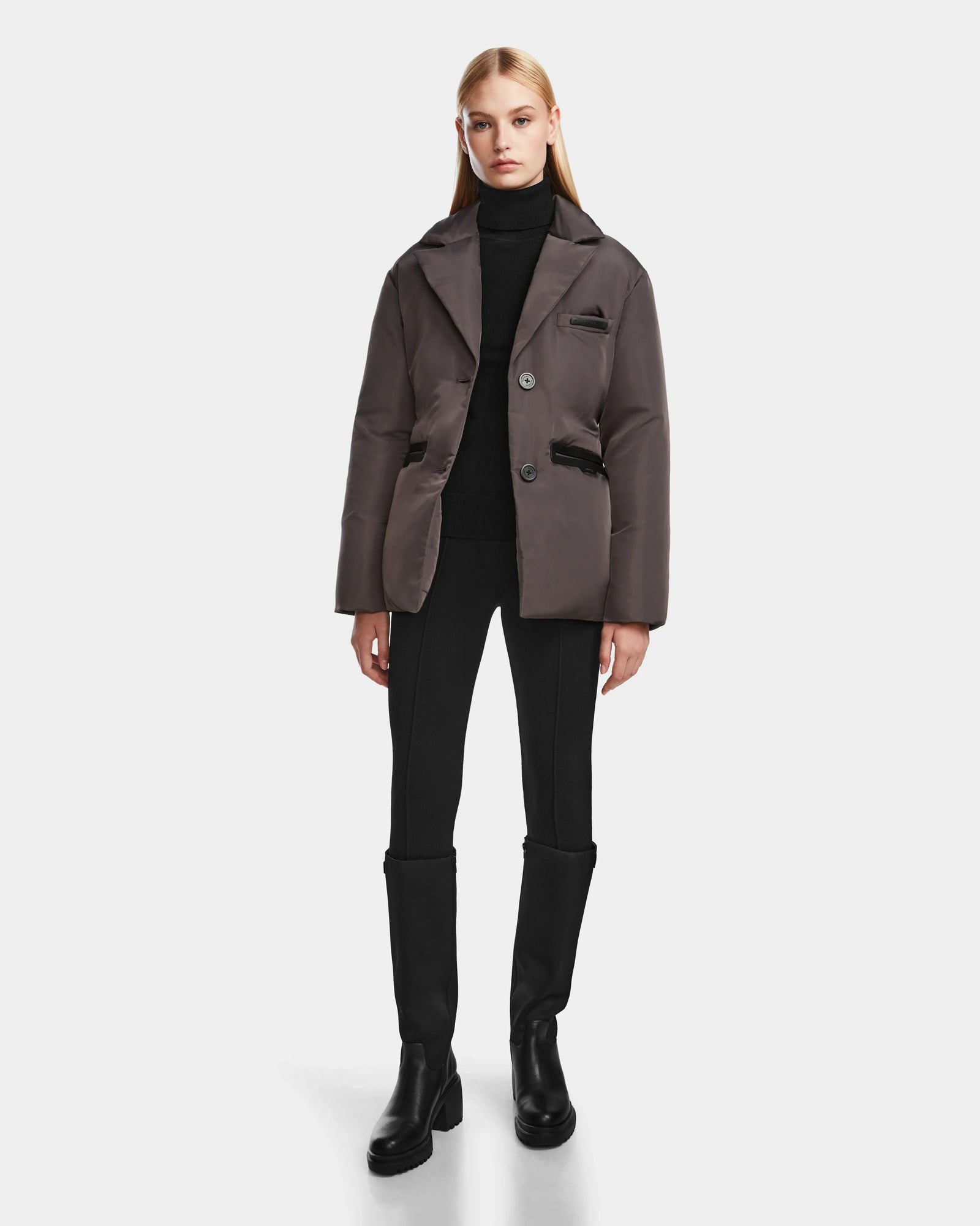 A woman with straight blonde hair models the Rudsak PAOLA - 8124547 Grey womens down blazer over a black turtleneck, fitted black pants, and black knee-high boots against a plain white background.