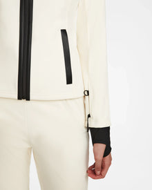 A person wearing Rudsak's ROSALIE - 8124784 Iceland high-performance off-white ski jacket with matching pants, showcasing black zipper and wrist details. Only the lower jacket half and right arm appear against a white background.
