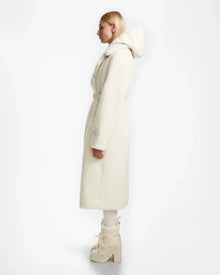 A person with straight blonde hair in profile models the Rudsak TINA - 8123578 Iceland womens trench coat with removable hooded bib and matching off-white high-heeled boots against a plain white background.