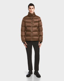 A person faces forward wearing the Rudsak VINCE S - 6124560 Antique Bronze mens quilted down puffer, paired with black pants and shoes, against a plain white background.