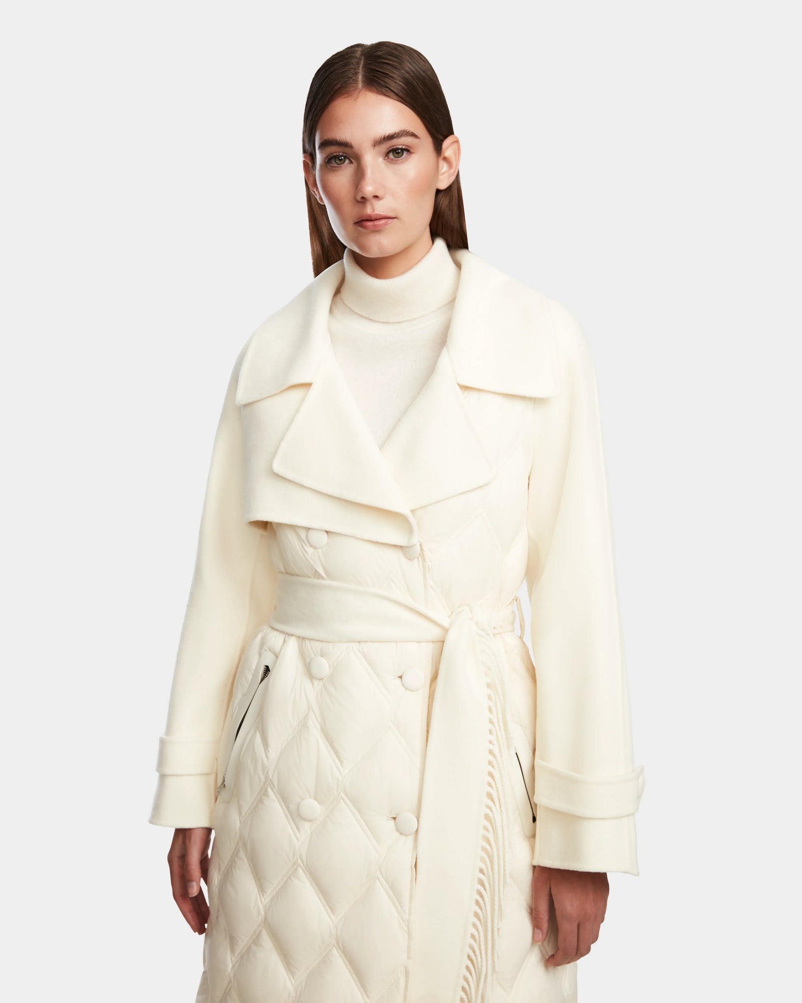 A woman with straight brown hair models the Rudsak ZOE - 8124711 Iceland cream long trench coat, featuring a wide collar, double-breasted buttons, and waist tie, paired with a matching turtleneck against a plain background.
