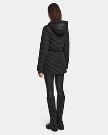 A person is seen from the back wearing the Rudsak FRANCINE - 8124722 Black quilted puffer jacket with a hood, paired with black leggings and tall black boots, set against a plain white background.