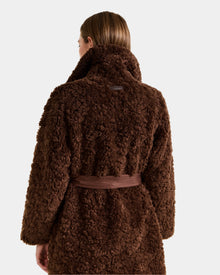A person with straight, light brown hair is shown from the back, wearing the Rudsak ANNABELLE FSU - L125512 Espresso sherpa teddy coat with a textured finish and matching belt tied at the waist.