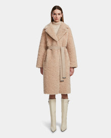 A woman faces forward, wearing the Rudsak ANNABELLE - L124544 Sand women's reversible teddy coat over a light turtleneck. Her straight hair and knee-high cream boots complete the look against a plain white background.
