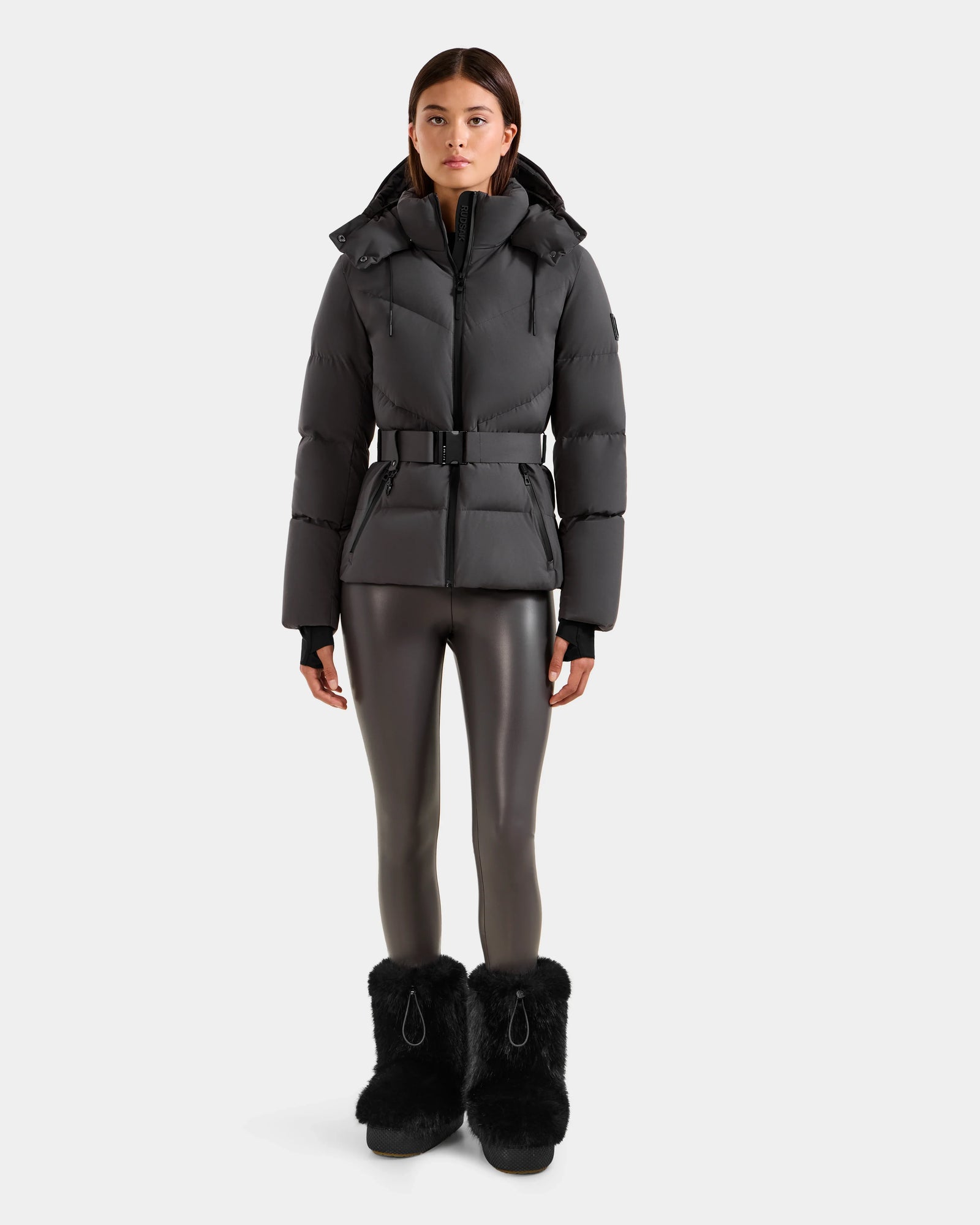 A woman stands facing forward, wearing the Rudsak CHRISTELLE M - L125542 Grey belted quilted down puffer jacket against a plain light background.