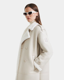 A woman in the Rudsak DARCY - L125539 Vanilla women's winter coat poses against a plain white background, wearing white sunglasses and a light turtleneck, looking confidently to the side.