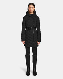 A woman faces forward wearing the Rudsak DITA - L124556 Black knee-length puffer jacket with a high collar and zippered front, paired with black pants and knee-high boots against a plain white background.