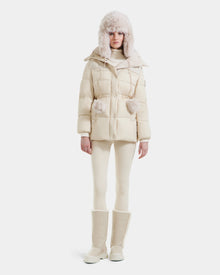 A person wearing the Rudsak EMBER M-M - L125524 Vanilla women's down puffer jacket with fur trim, plus a matching fur hat, leggings, and tall fur-lined boots in cream, stands against a plain white background.