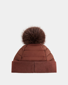 The GALA - 8424514 Rust by Rudsak is a brown quilted winter hat with a wide cuff and a large, removable faux fur pom pom, shown against a plain white background.
