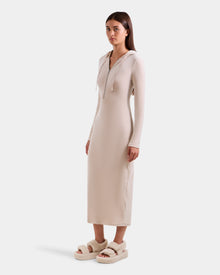A woman in a long, fitted velour hooded dress with a front zipper stands slightly to the side, wearing Rudsak's ISABELLA - L525502 Cream platform sandals with thick, fuzzy straps.