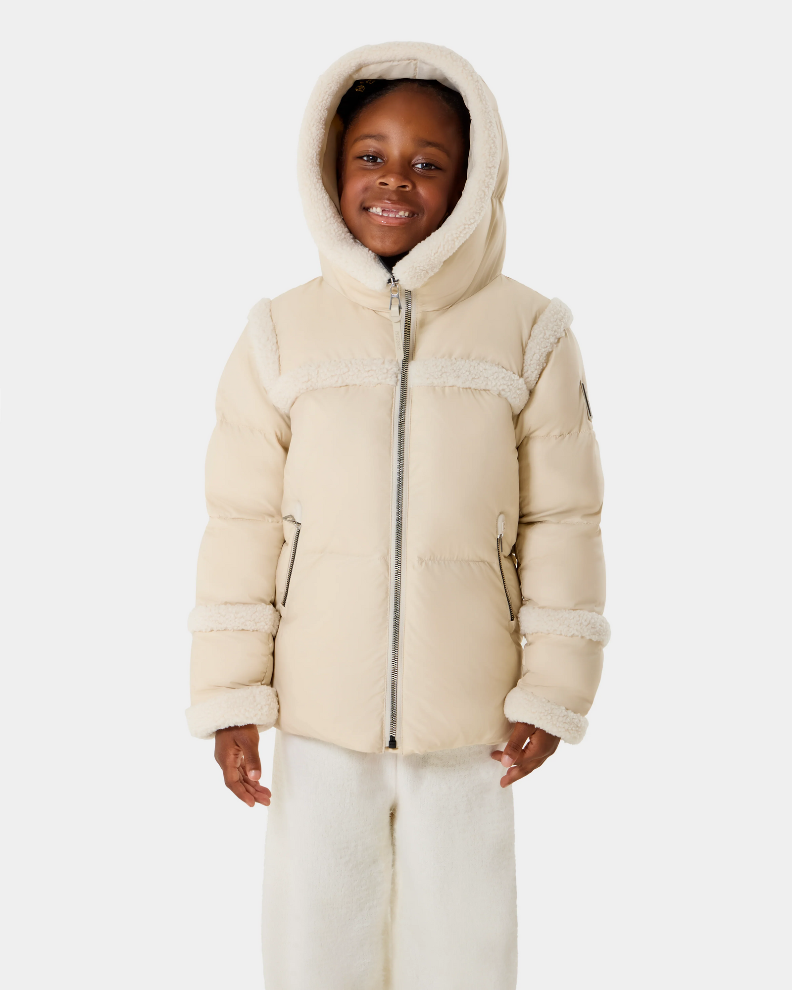 A young child models the Rudsak JULIANA K - K125550 Vanilla, a cream hooded winter jacket with faux fur trim and matching light pants, smiling against a plain white background.