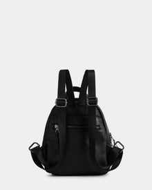 The Rudsak KATTY - L325014 Black mini backpack is shown from the back in black pebbled leather, featuring adjustable shoulder straps, a rear zip pocket, and silver hardware against a plain light grey background.