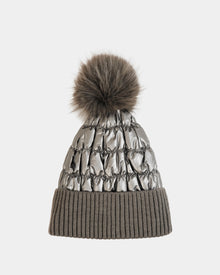 The LANYA - L423514 Pewter by Rudsak is a silver-toned winter hat with ruched details, a large brown pom-pom, and a wide ribbed taupe brim, set against a plain white background.