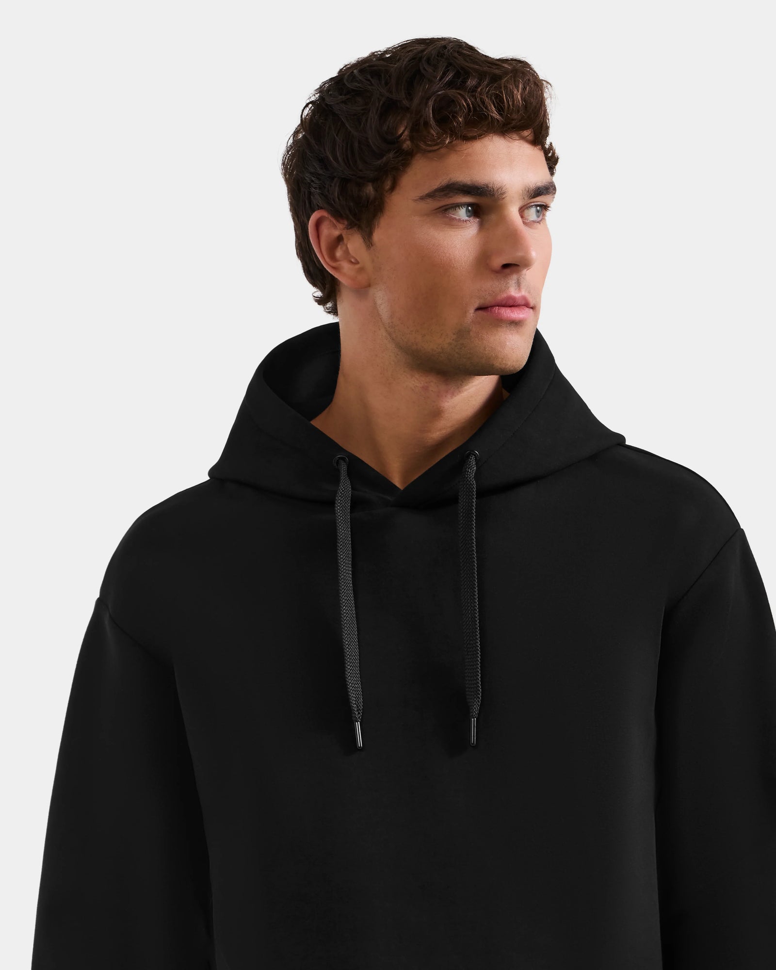 A young man with short curly brown hair wears the Rudsak LEROY - U525509 Black M hoodie and looks slightly to the side against a plain light background.