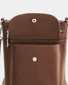 Close-up of the Rudsak LILA - L325513 Mocha crossbody bag, shown in brown pebbled leather with its front flap open. Features include a silver snap button closure, exterior pocket with snap, and a detachable strap with metal clasp.