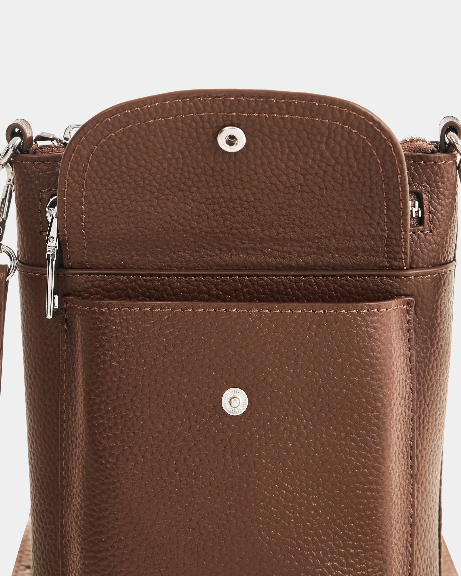 Close-up of the Rudsak LILA - L325513 Mocha crossbody bag, shown in brown pebbled leather with its front flap open. Features include a silver snap button closure, exterior pocket with snap, and a detachable strap with metal clasp.