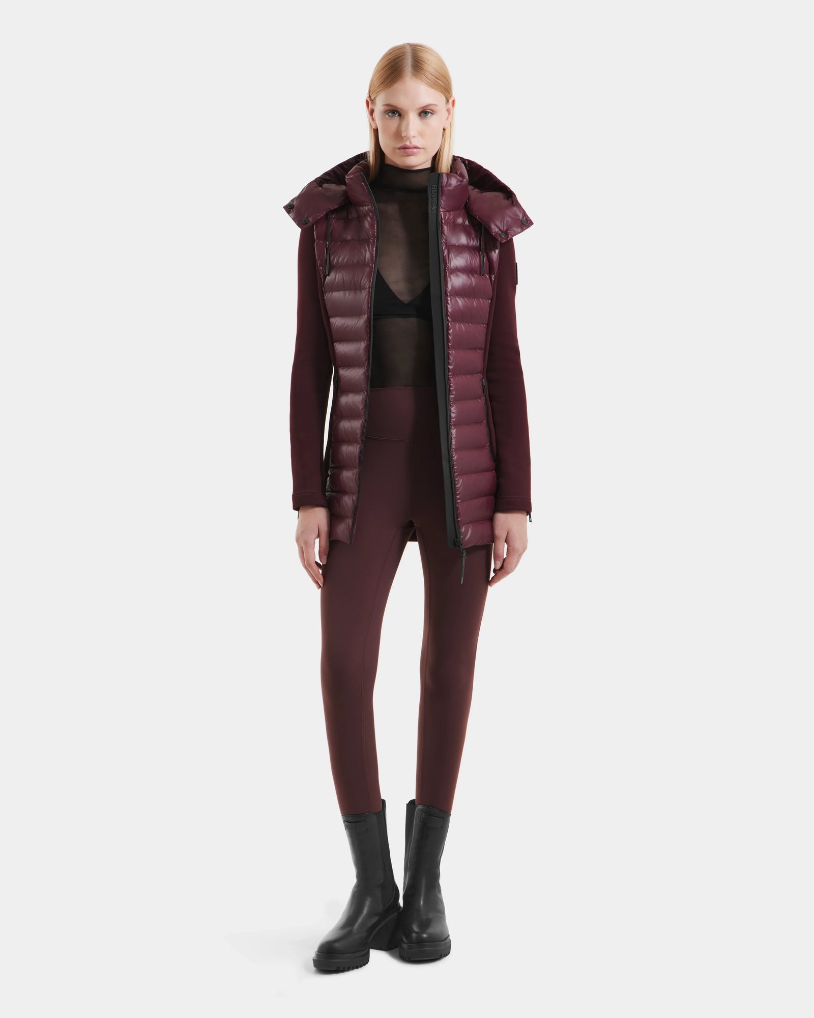 A woman stands facing forward wearing the Rudsak MARRY S - L125521 Wine weather-resistant puffer vest, a sheer black top, burgundy fitted pants, and black ankle boots against a plain white background.