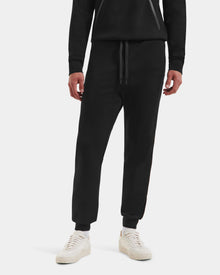 Wearing Rudsak's MAXTON - U525007 Black M jogger sweatpants, this person stands against a plain white background. Only the lower half is visible, highlighting everyday comfort in sleek black athleisure style.