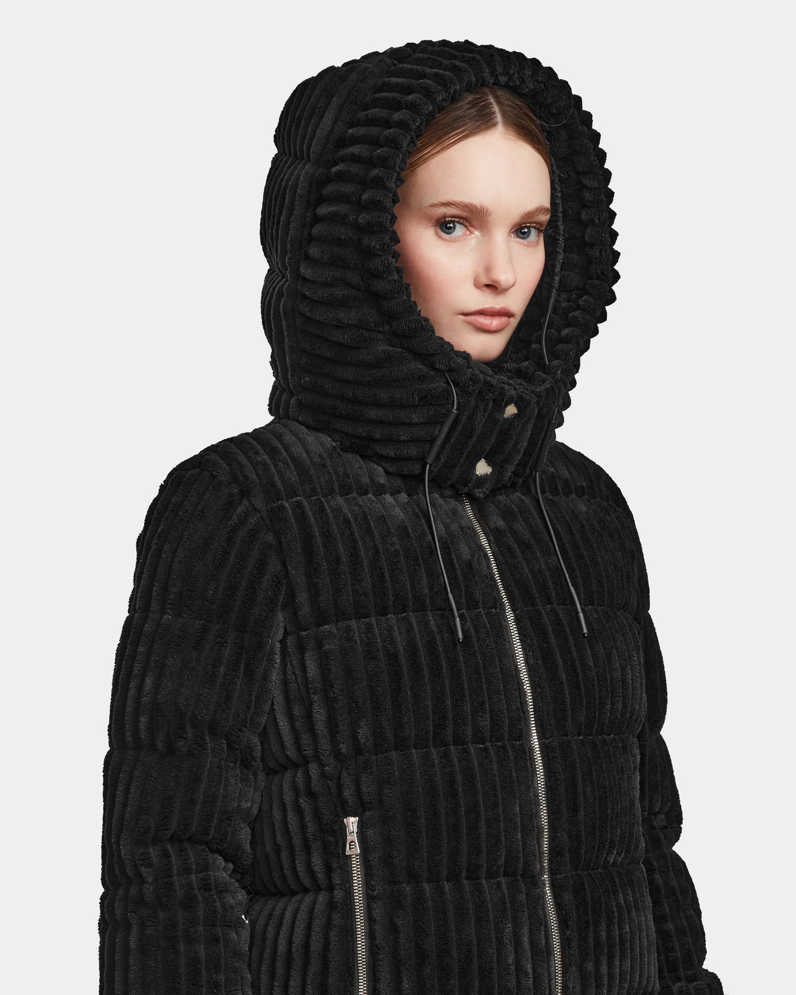 A woman wears the MIRRY FF - L124507 Black short down puffer jacket with a large hood and zipper closure, looking slightly to the side against a plain white background.