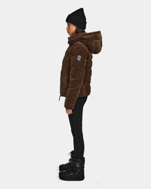 A person in profile models the Rudsak MIRRY FF - L124507 Espresso velvet corduroy puffer with a hood, paired with a black knit beanie, black pants, and black winter boots against a plain white background.