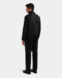 A man, seen from behind, wears the REYMOND M - M125523 Black men’s down jacket by Rudsak, made of recycled nylon, with black pants and shoes against a plain light gray background.