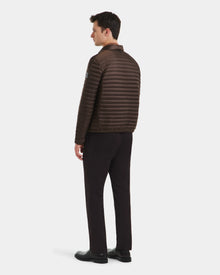 A man faces away, wearing the Rudsak REYMOND M - M125523 Mocha brown quilted puffer men's down jacket in recycled nylon, paired with black pants and shoes, against a plain white background.