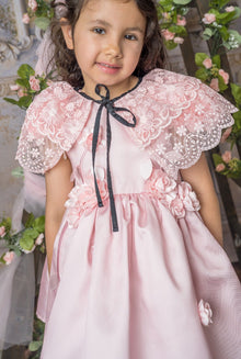 Girl wearing blush pink lace cape accessory with a black waist bow detail, paired with a satin pink dress for an elegant look