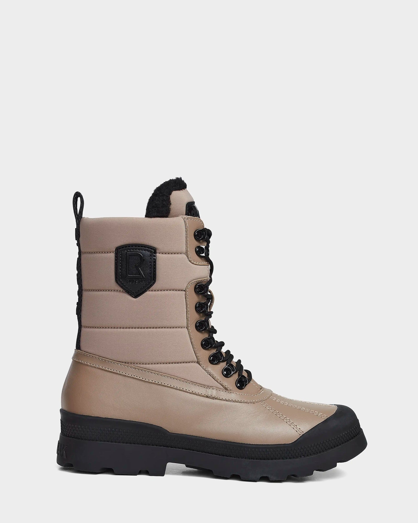 The REAGAN - 6222500 Cement by Rudsak is a men’s winter boot in tan and black, with thick rubber sole, lace-up front, black eyelets, back loop, quilted insulated design, waterproof finish, and a black “R” patch on the side.