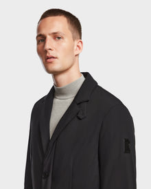 A young man with short hair wears the Rudsak OTTO - 6124602 Black mens blazer-style down jacket over a light gray turtleneck, looking slightly left with a neutral expression against a plain white background.