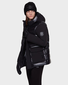 A person wears the Rudsak DUSK - M121506 BLACK puffer jacket, paired with black gloves and a beanie, standing against a plain white background and gazing slightly to the side with a neutral expression.