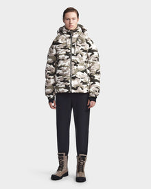 A person stands facing forward against a plain light background, wearing the Rudsak VINCENT M - 6123510 Camouflage men's down puffer in black-and-white camo, paired with black pants and tan lace-up boots.